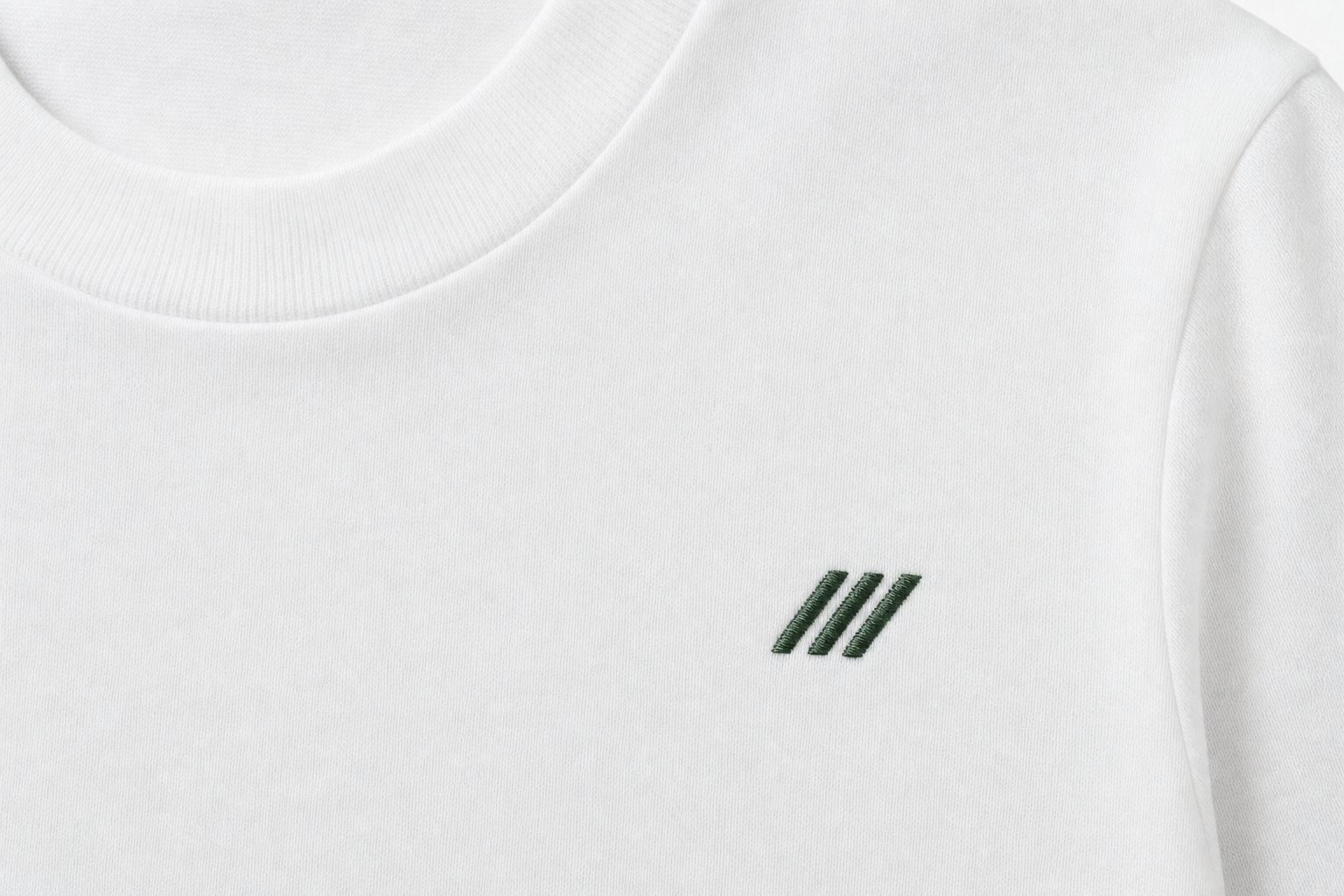 Gros plan sur une broderie vert foncé en points de bourdon sur un t-shirt blanc en jersey de coton