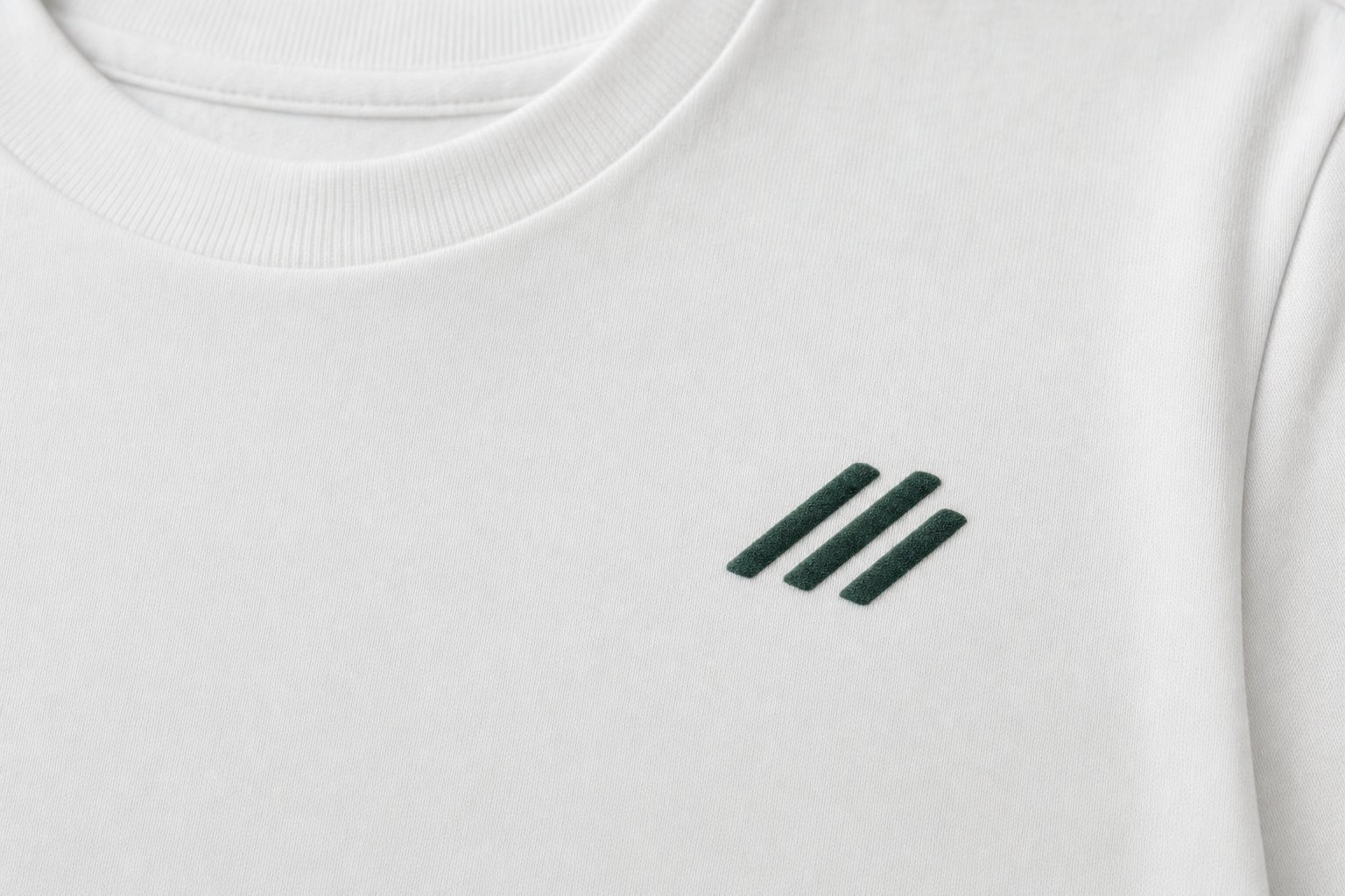 Gros plan sur un emblème vert foncé en film floqué mat, aux bords nets, sur un t-shirt blanc